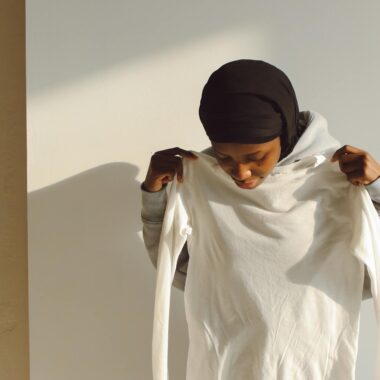 A young woman trying on a white long-sleeve shirt indoors under bright light.