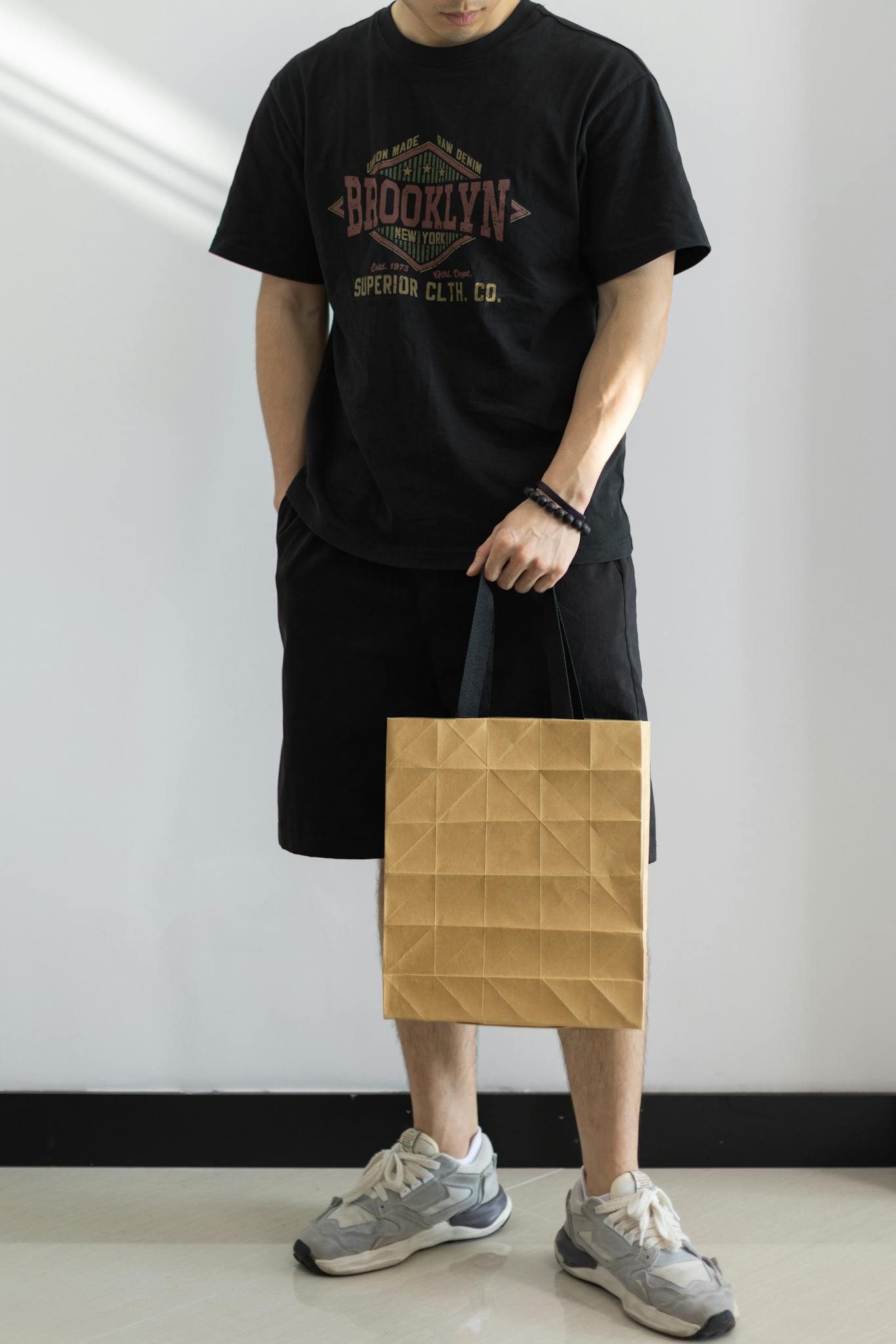 Young man standing indoors holding a textured shopping bag.